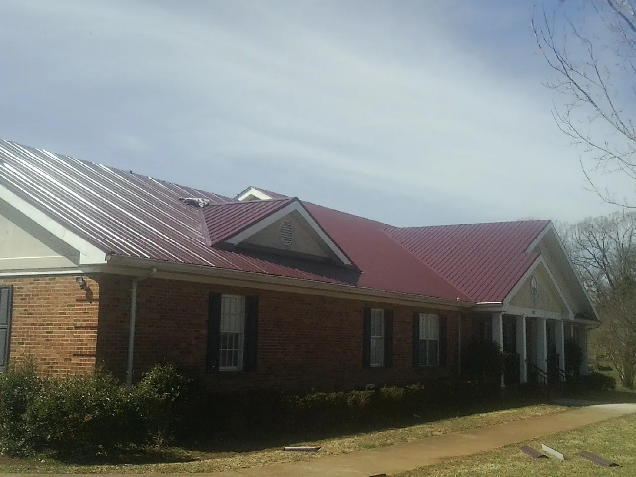 Red metal roof with gabled entries on a long brick building, from a Hail Damage Roof Repair job in Tulsa
