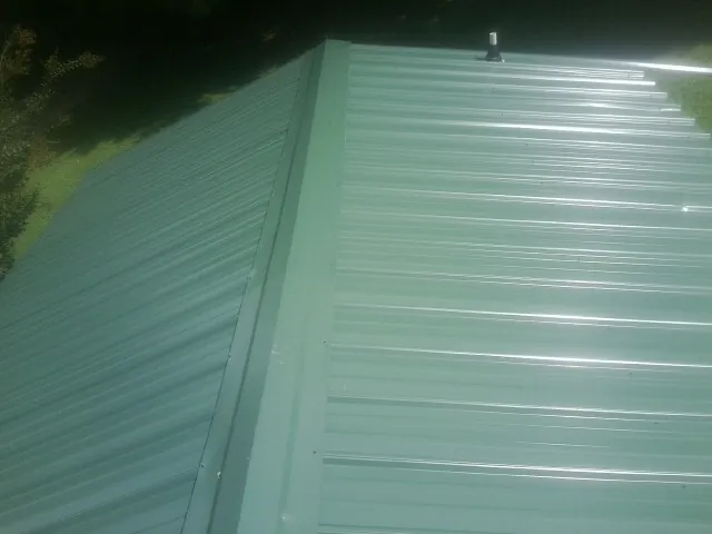 New green metal panels meeting at the ridge of a roof — Flat Roof Repair work by our crew in Tulsa