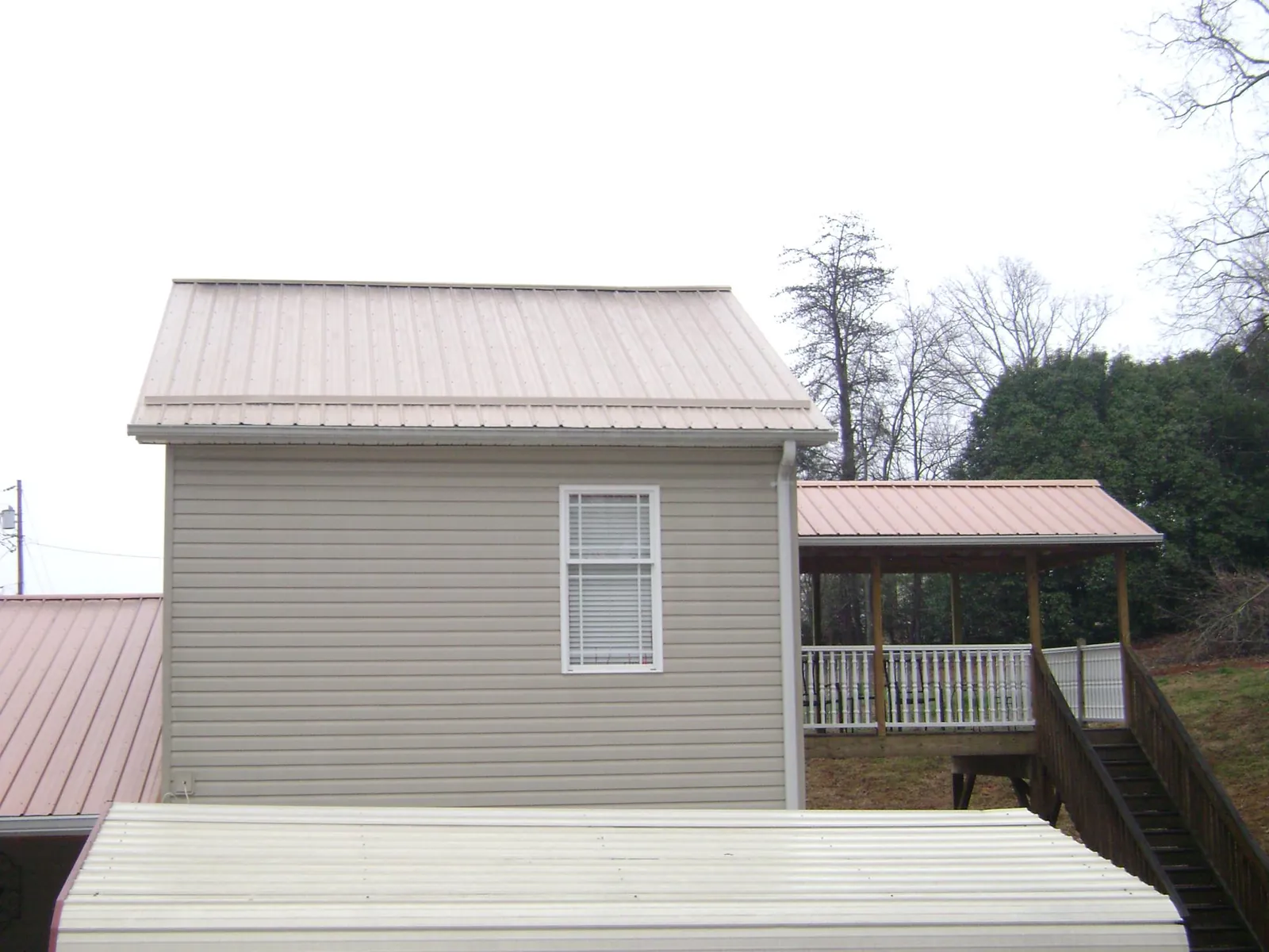 Tan metal roofs on a two story addition and attached porch, from a Roof Replacement job in Tulsa