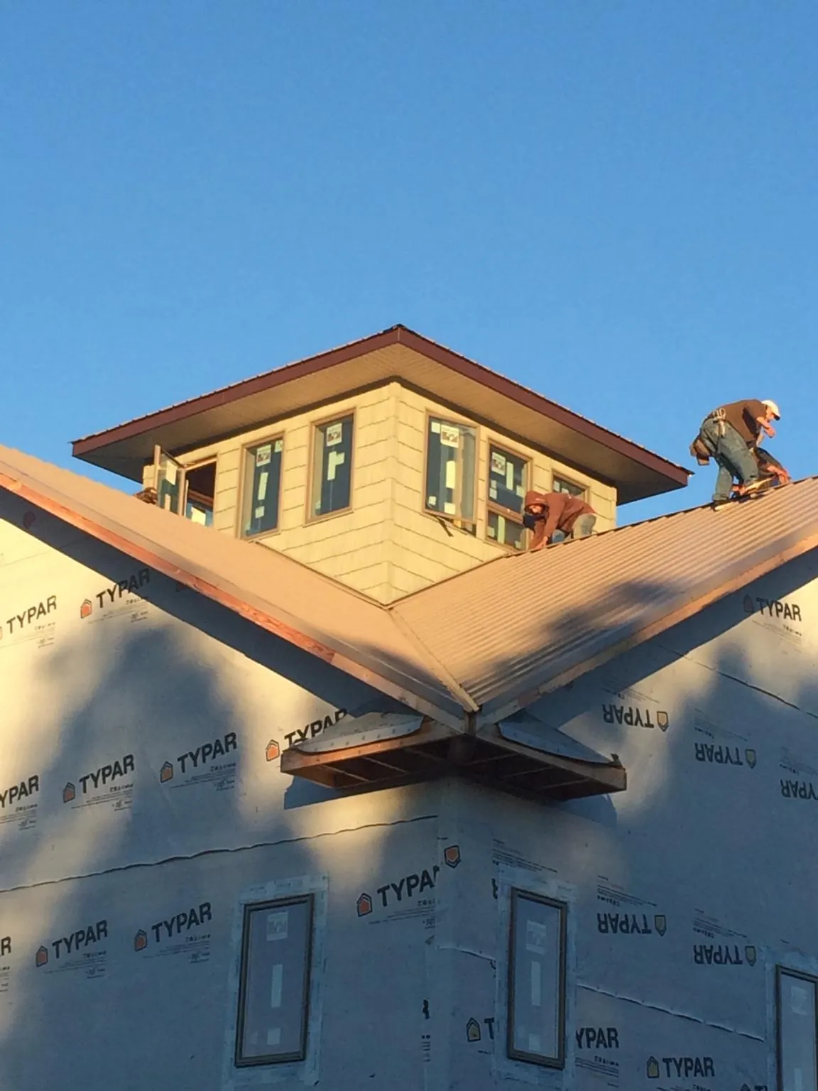 Roofers working around a rooftop cupola on a new metal roof at sunset — Roof Waterproofing in Tulsa by Roofing Brothers